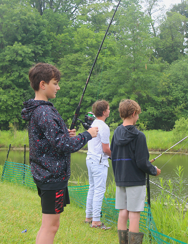 Three young boys fish in the grass at the WWK pond.